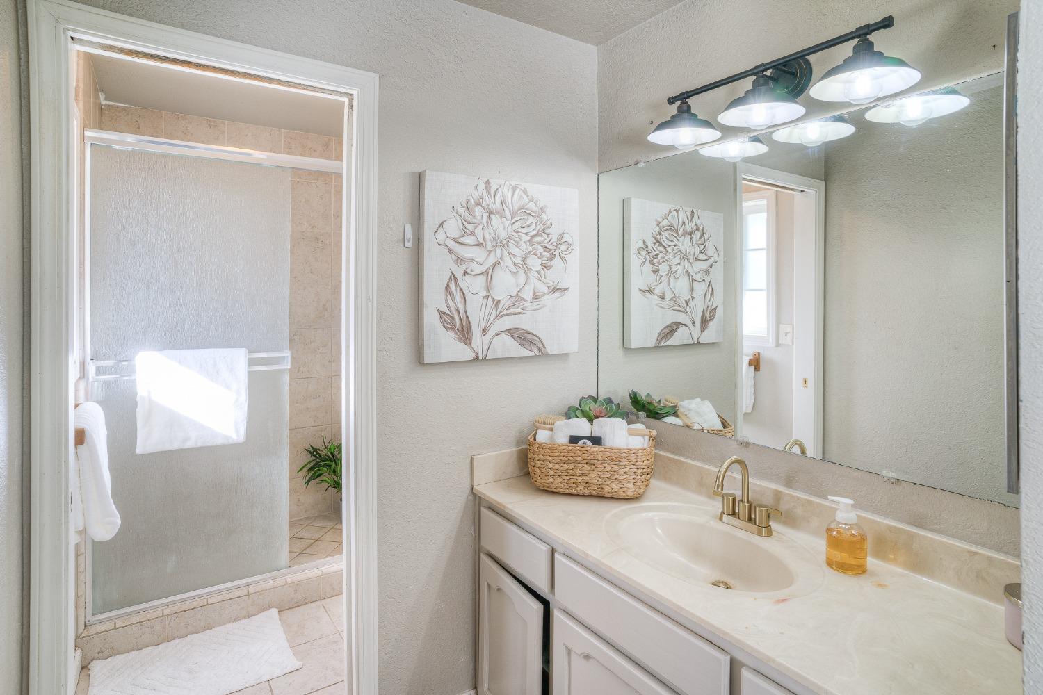 Bathroom with a white vanity and brass faucet beside a tiled glass shower.