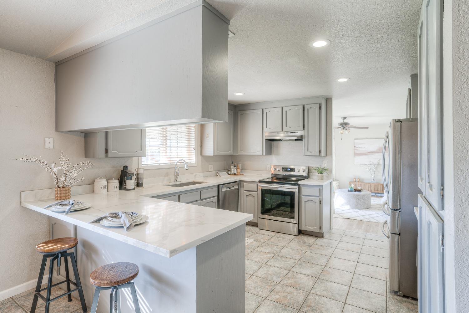 Kitchen with gray cabinets, stainless steel appliances, and a white breakfast bar with stools.