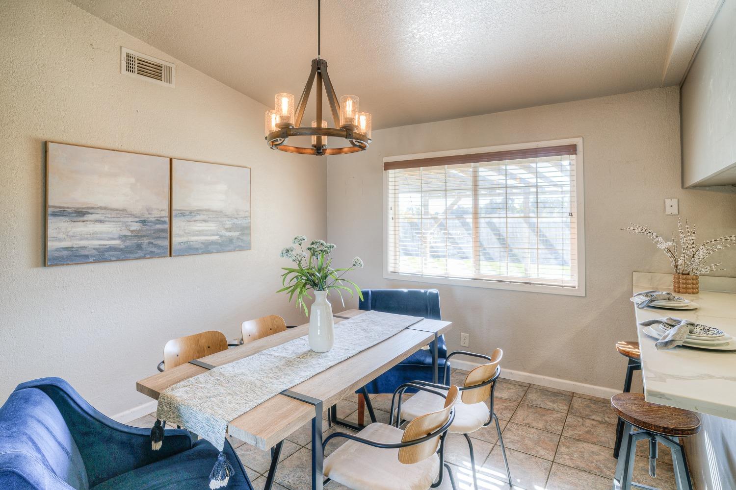 Dining room with a wood table, blue chairs, tiled floor, and a large window with blinds.