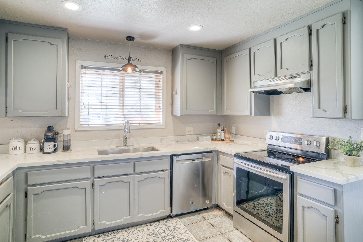 Kitchen with gray cabinets, white countertops, a window over the sink, and stainless steel appliances.