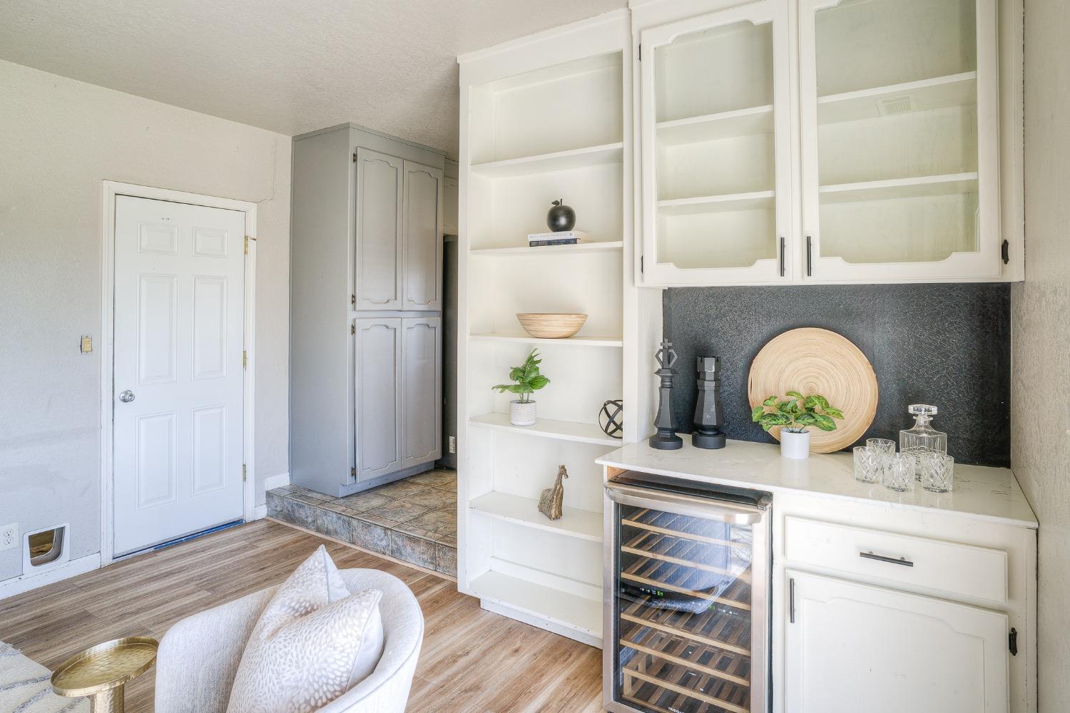 Staged wet bar with white cabinetry, open shelves, dark backsplash, and glass-front wine refrigerator.