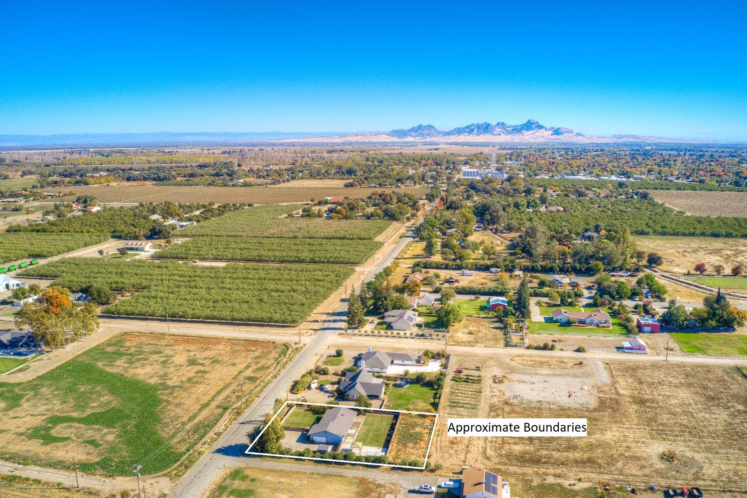 Aerial view of home and lot outlined by approximate boundaries, with orchards and distant mountains.