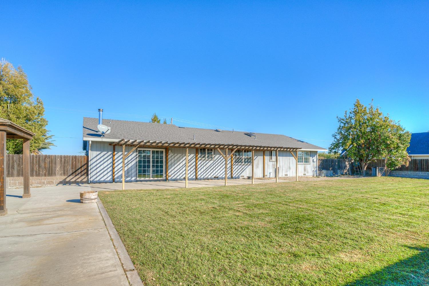 Rear of a single-story house with a covered patio overlooking a broad grassy backyard.