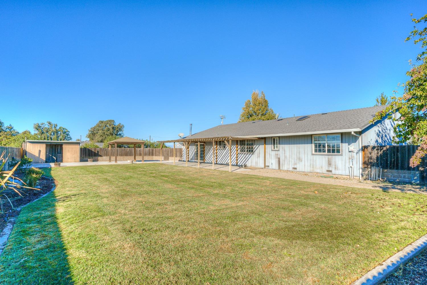 Backyard with a broad lawn, covered patio, and detached shed behind a single-story home.