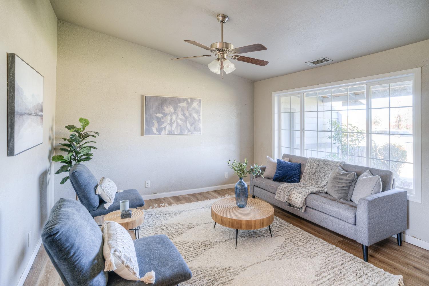 Staged living room with gray sofas, blue chairs, a round wood coffee table, and large grid windows.