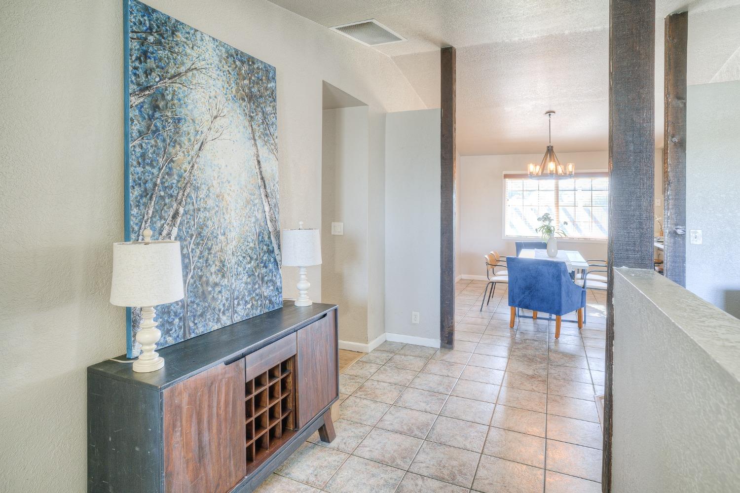 Tiled entryway opens to a dining area, with a dark console and large blue tree artwork.