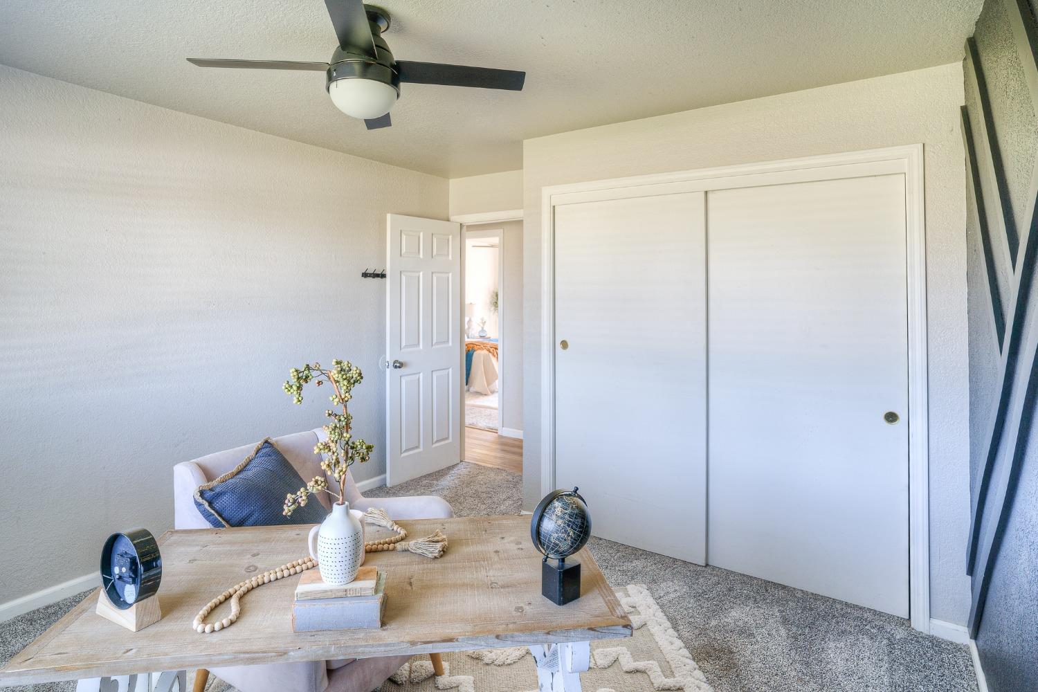 Staged room with a wood desk, cushioned chair, ceiling fan, and large sliding-door closet.