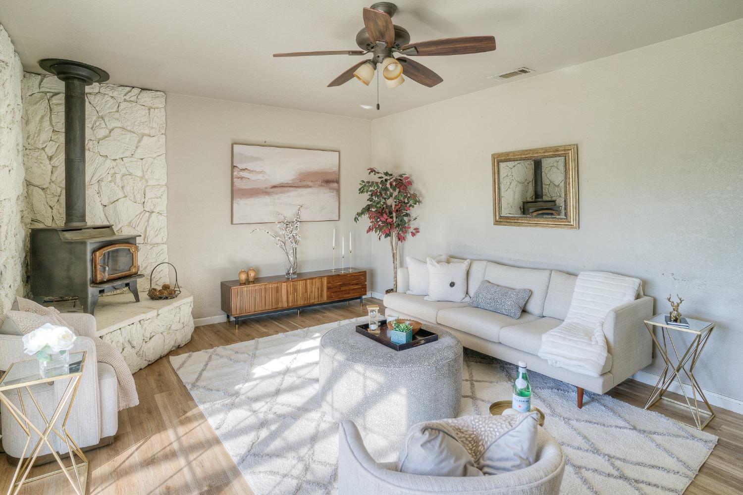 Living room with a white sectional, stone fireplace and wood stove, and sunlight across the rug.