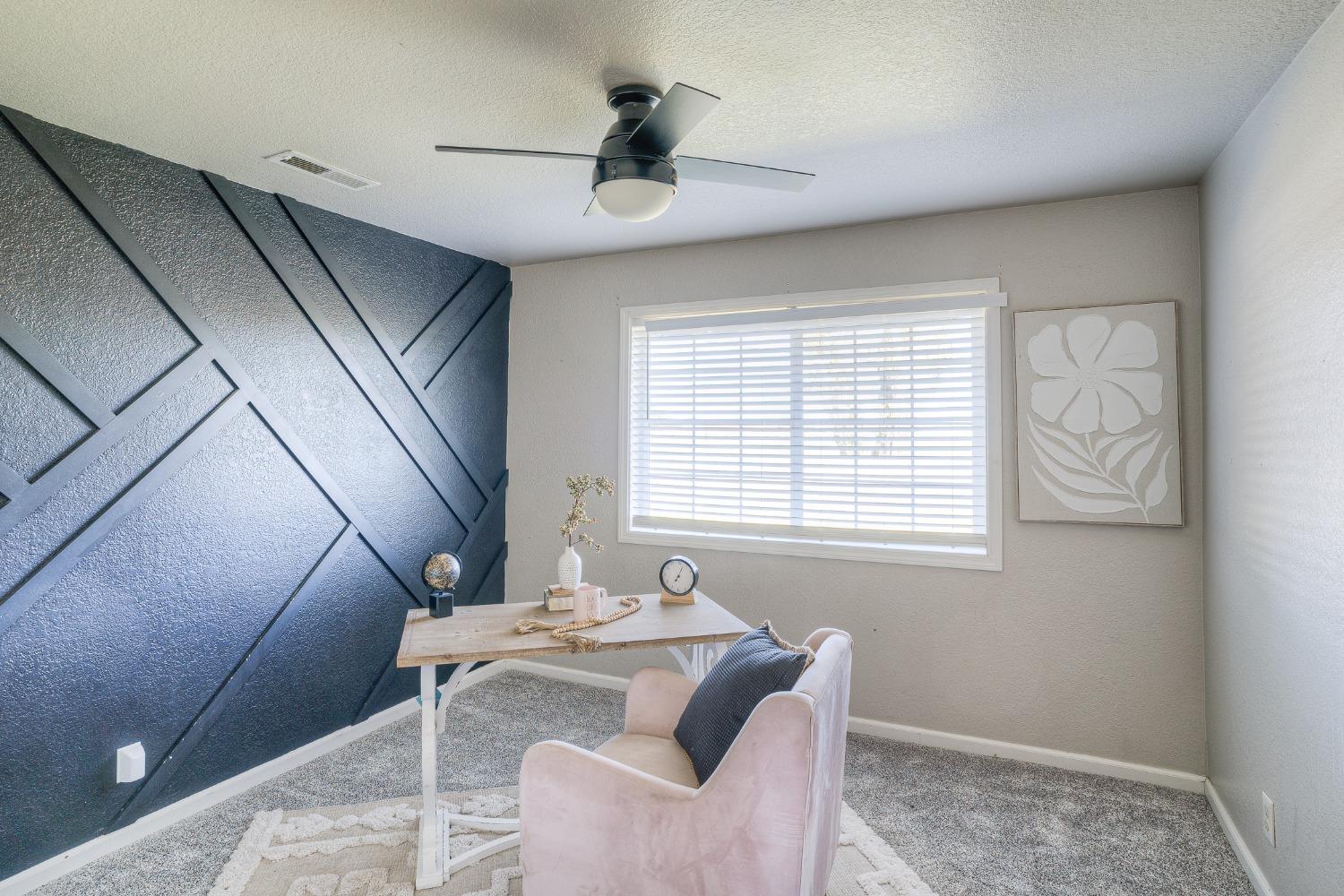 Home office with a blue geometric accent wall, light wood desk, and blush chair.