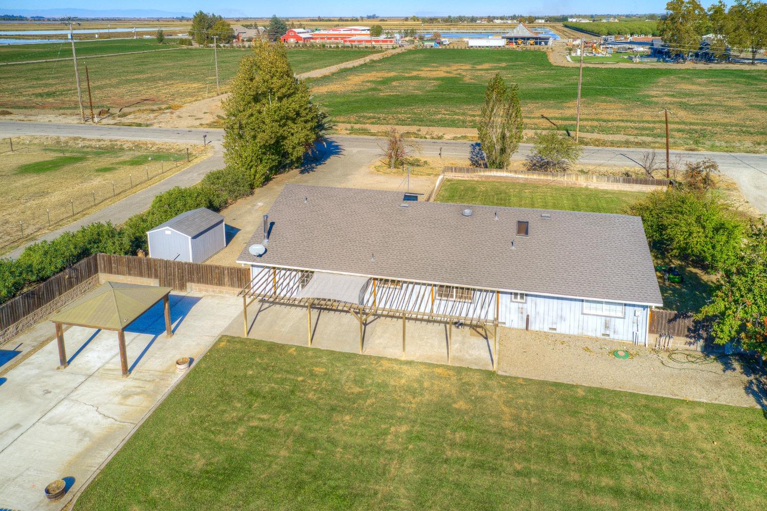 Aerial view of a home’s rear yard, covered patio, detached shed, and surrounding fields.