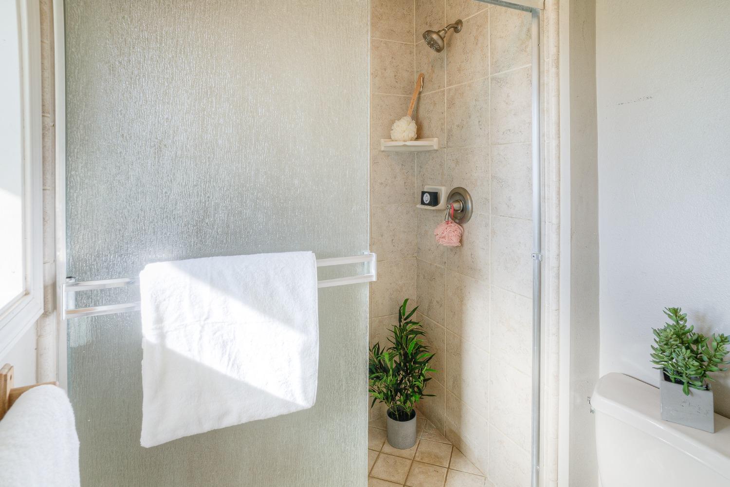 Bathroom shower with textured glass doors, beige tile, and a white towel.