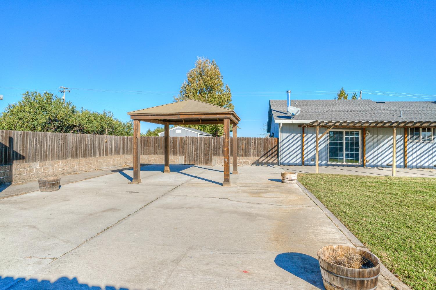 Backyard patio with a wooden gazebo beside the house and a small lawn.