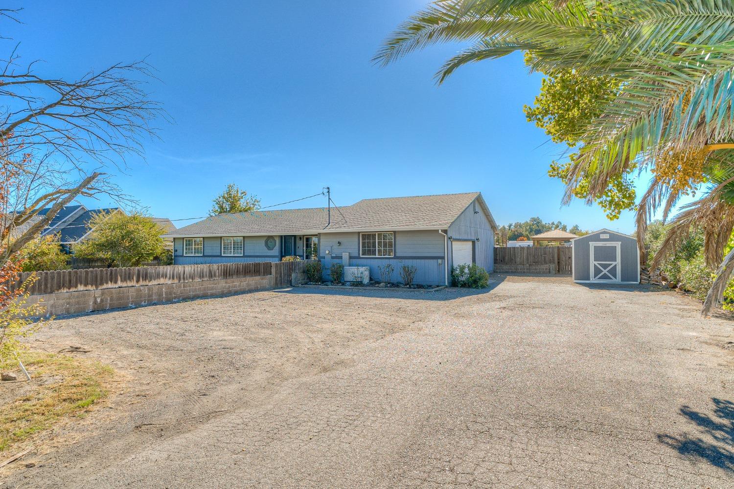 Single-story blue-gray house with a wide gravel driveway and detached storage shed.