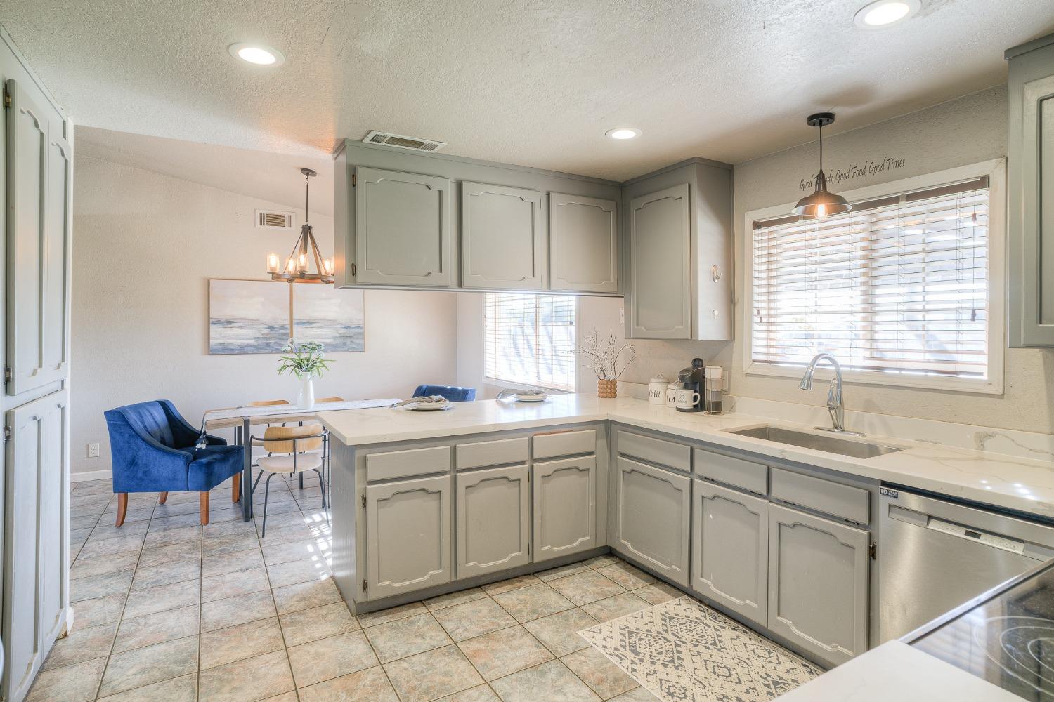 Kitchen with gray-green cabinets, white counters, and a breakfast bar beside a dining nook.