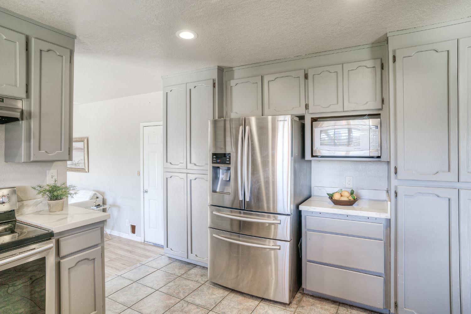 Kitchen with gray cabinets, stainless steel refrigerator, and built-in microwave.