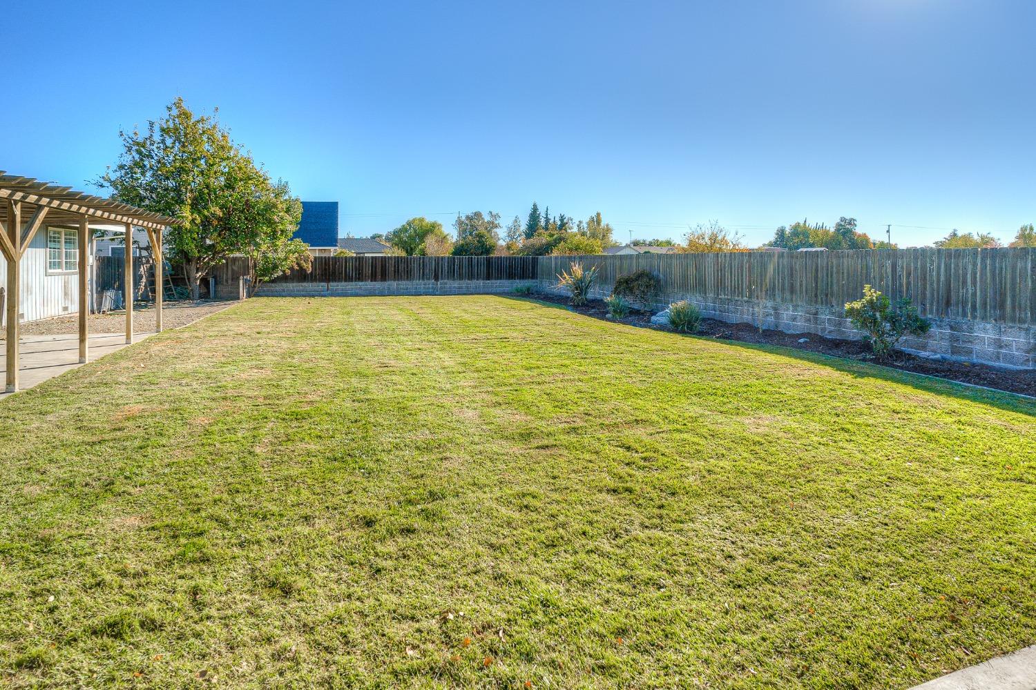 Fenced backyard with a broad lawn, wooden pergola, and planted border.