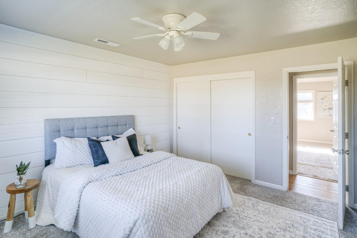 Bedroom with a white quilted bed, paneled accent wall, and ceiling fan.