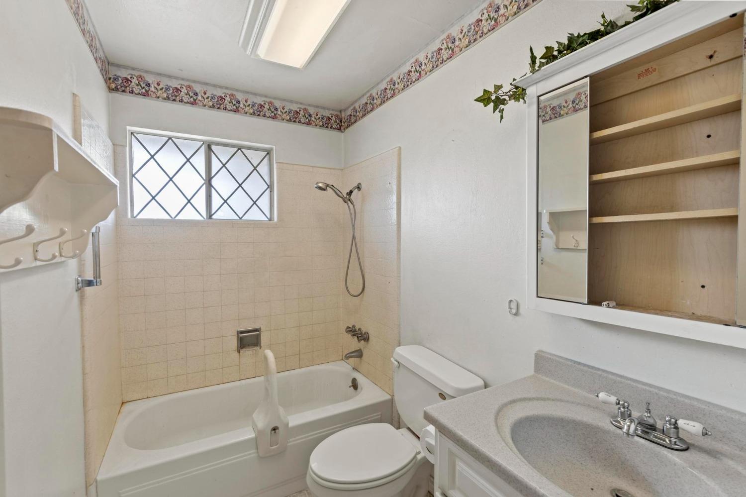 Bathroom with a tiled tub and shower, diamond-pane window, and mirrored vanity cabinet.