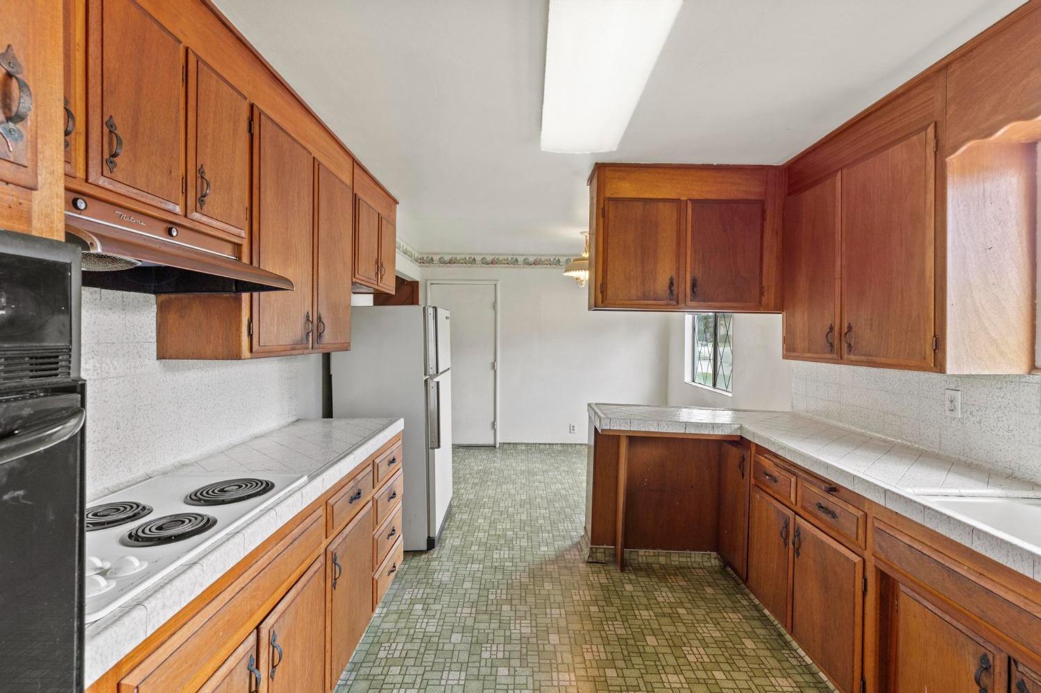 Kitchen with wood cabinets, tiled counters, an electric range, and green patterned flooring.