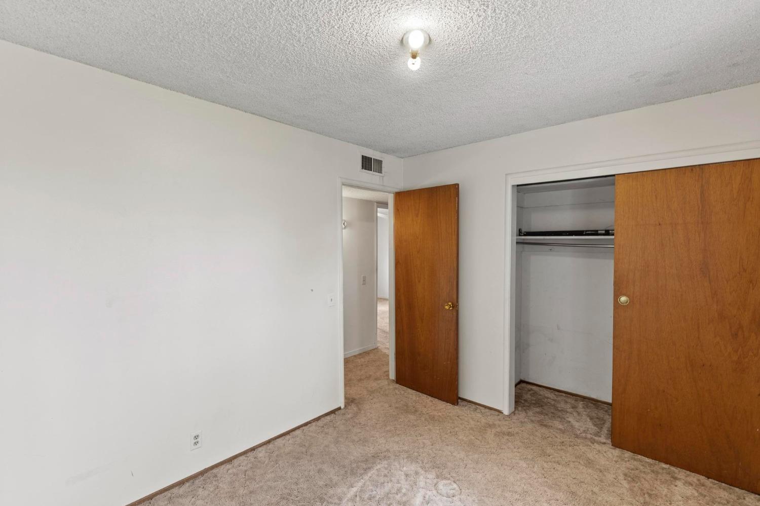 Empty bedroom with beige carpet and an open closet with wooden sliding doors.