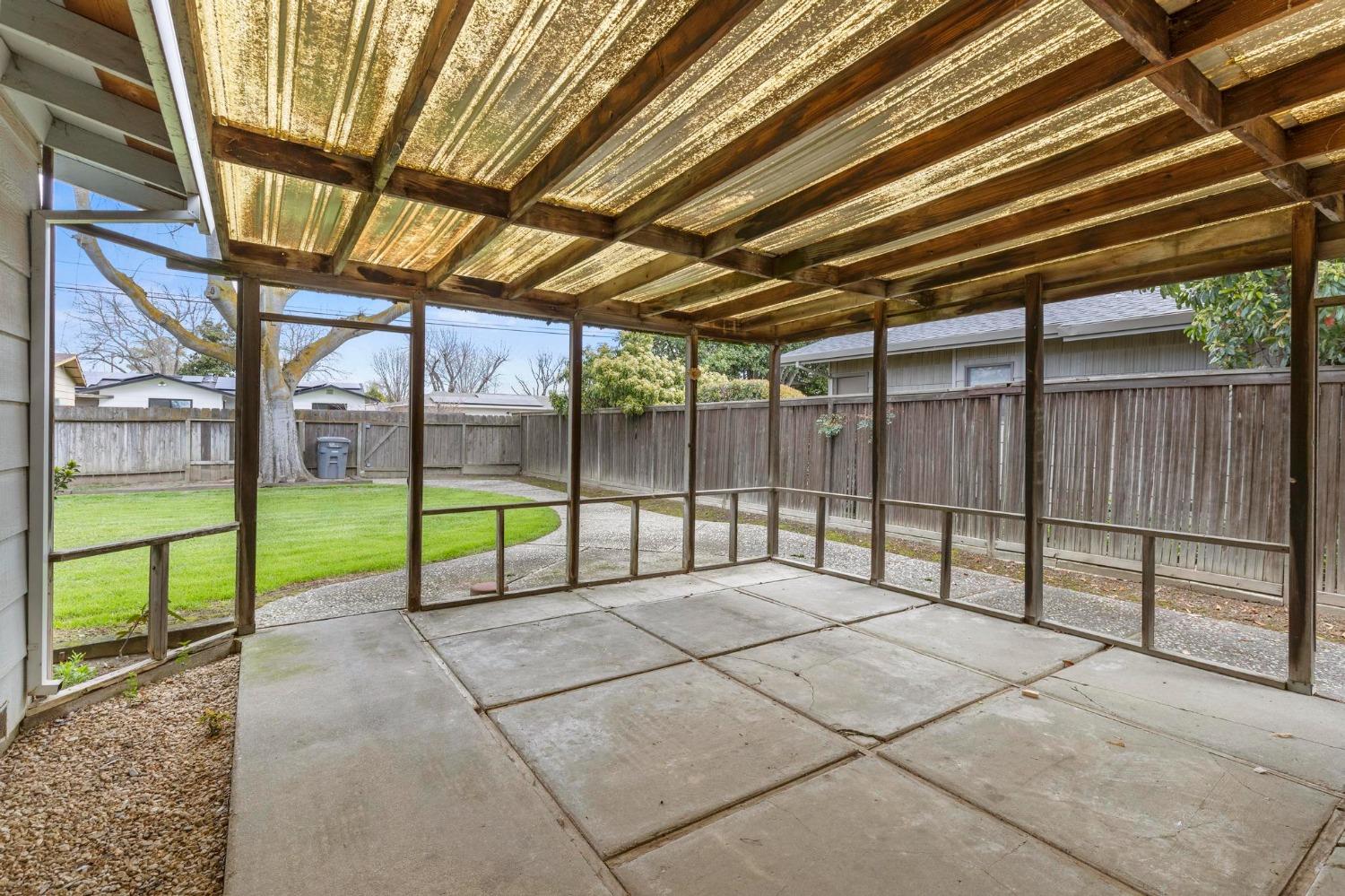 Covered backyard patio with exposed wooden beams, concrete flooring, and a view of the lawn.
