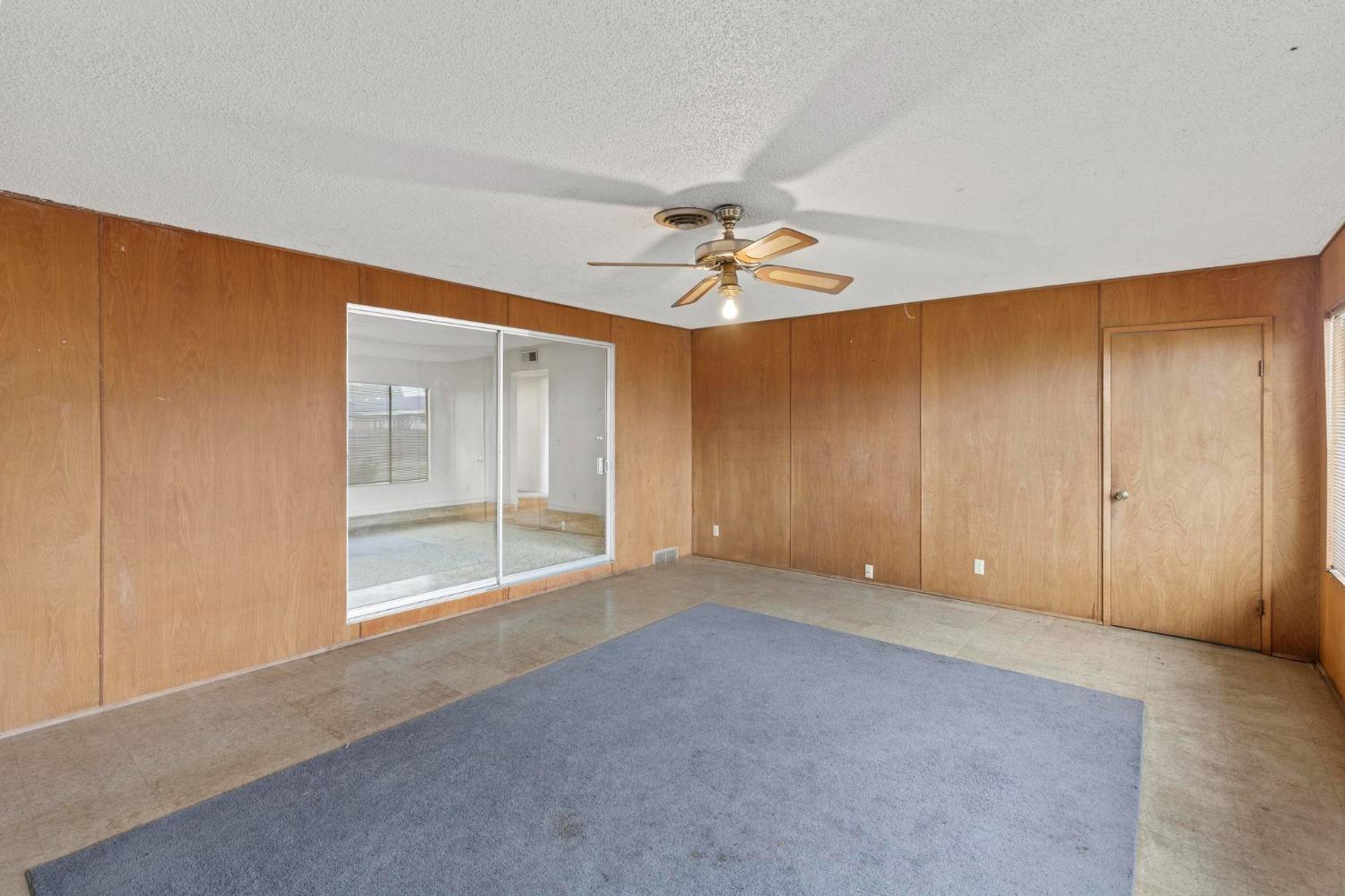 Empty room with wood-paneled walls, mirrored closet doors, and a large blue-gray carpet.