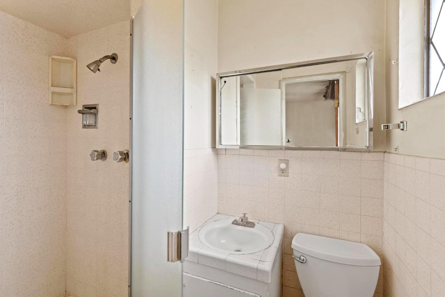 Bathroom with a tiled shower, sink, toilet, and wide mirrored medicine cabinet.