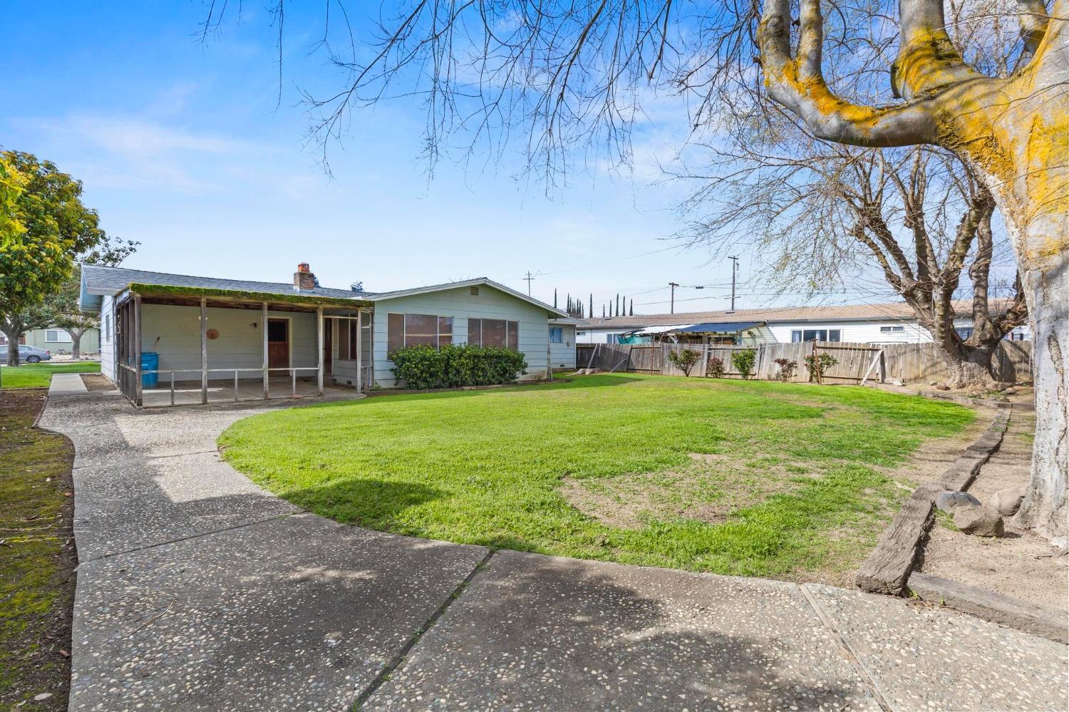 Single-story home with covered patio and broad green backyard beneath a large leafless tree.