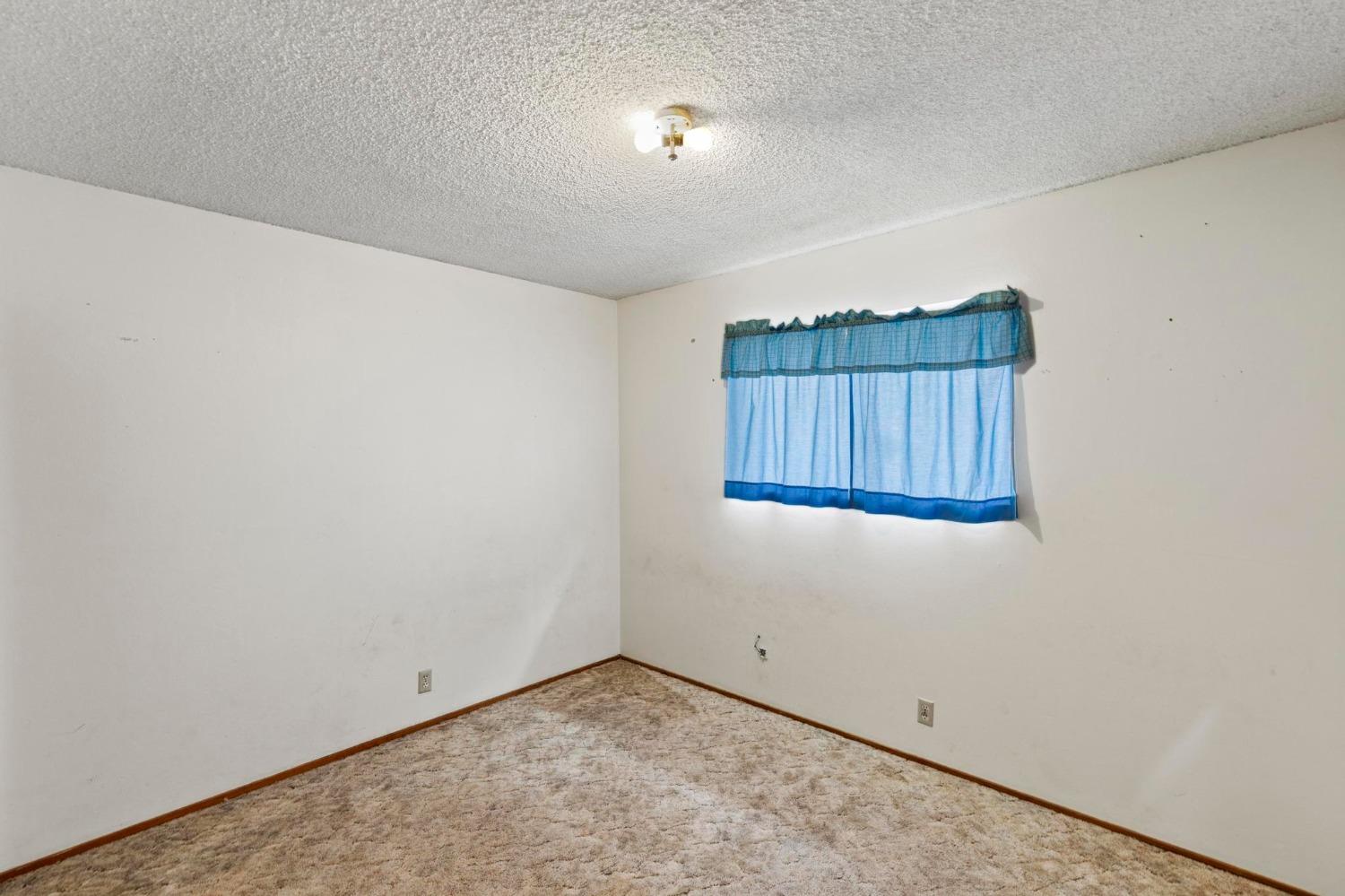 Empty carpeted room with blue curtains over a window and a ceiling light.