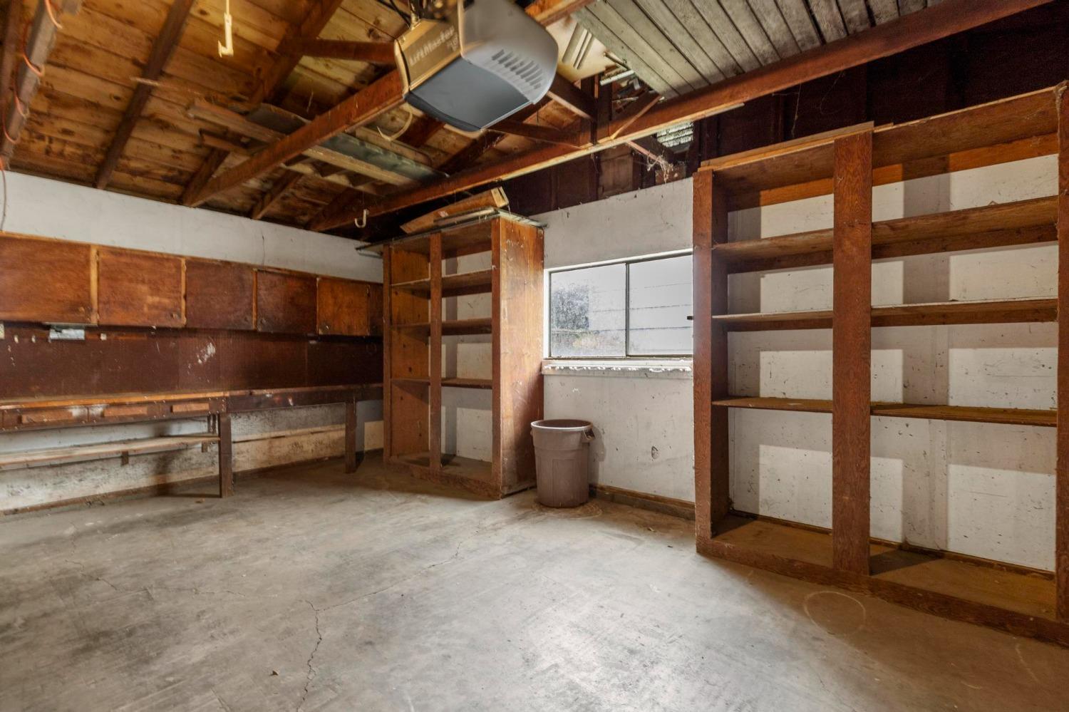 Garage with exposed rafters, built-in wooden shelves, and a bare concrete floor.