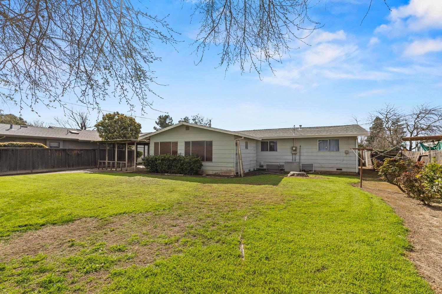 Single-story house viewed from the backyard, with a broad lawn and fenced yard.