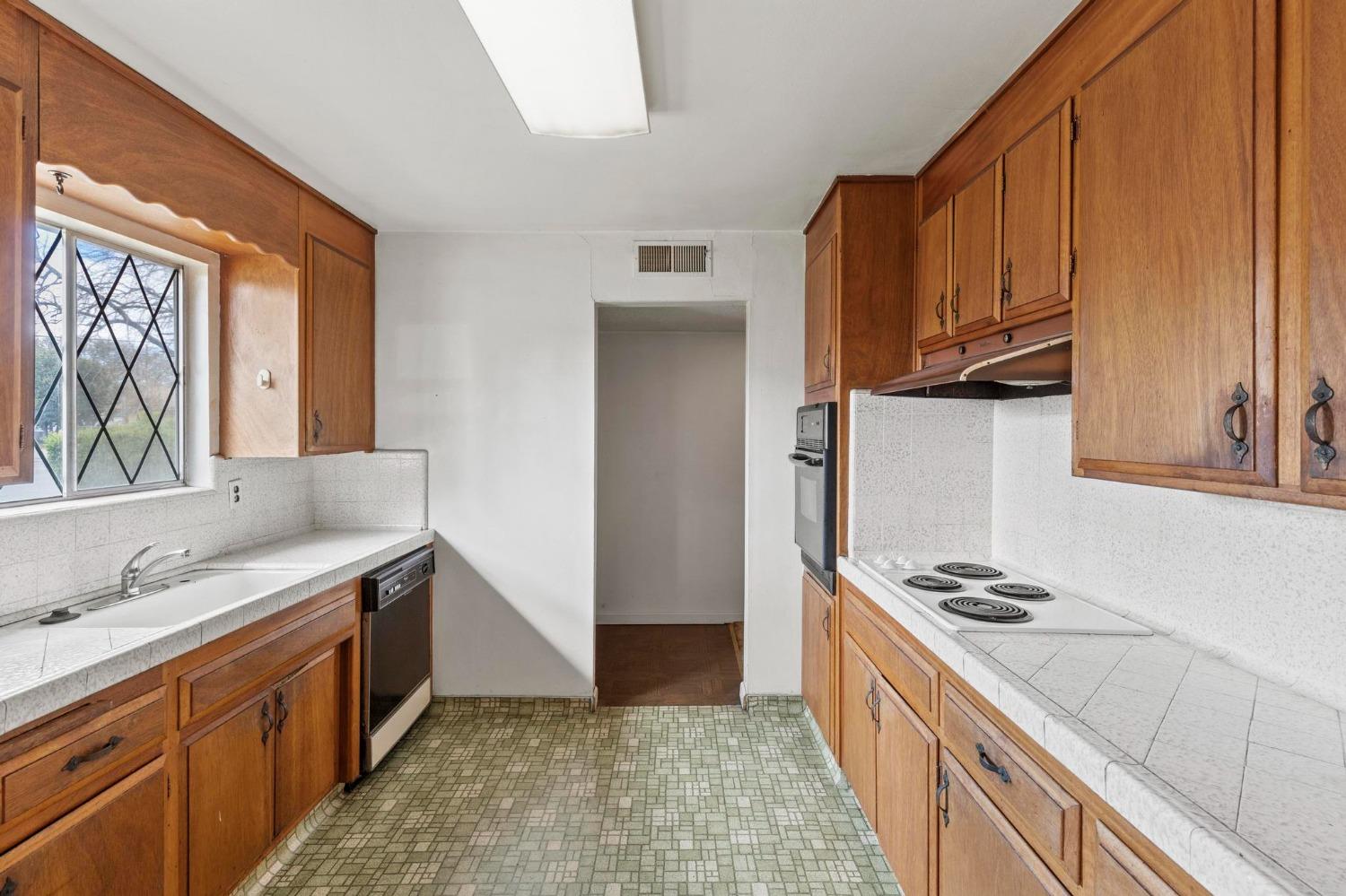 Kitchen with warm wood cabinets, white tiled counters, and a green patterned floor.