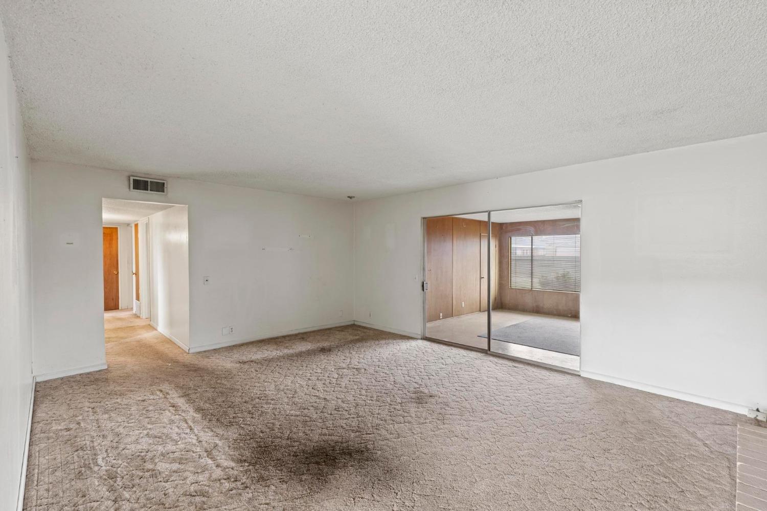 Empty carpeted living room with mirrored sliding doors to a wood-paneled adjoining room.