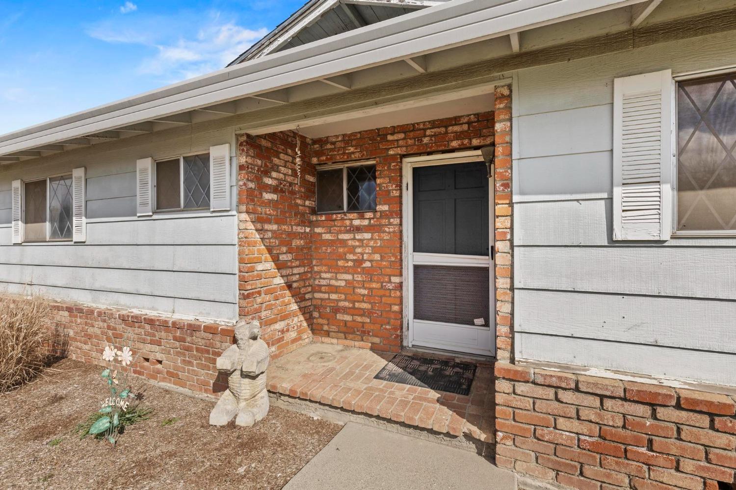 House entrance with pale gray siding, a recessed brick entry, and a small stone statue.