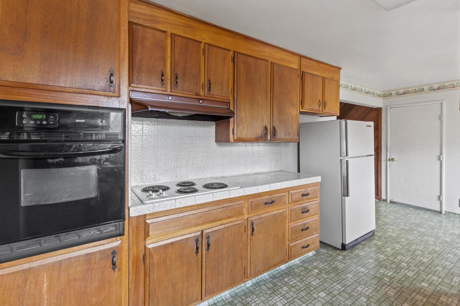 Kitchen with warm wooden cabinets, built-in oven, electric cooktop, and white refrigerator.
