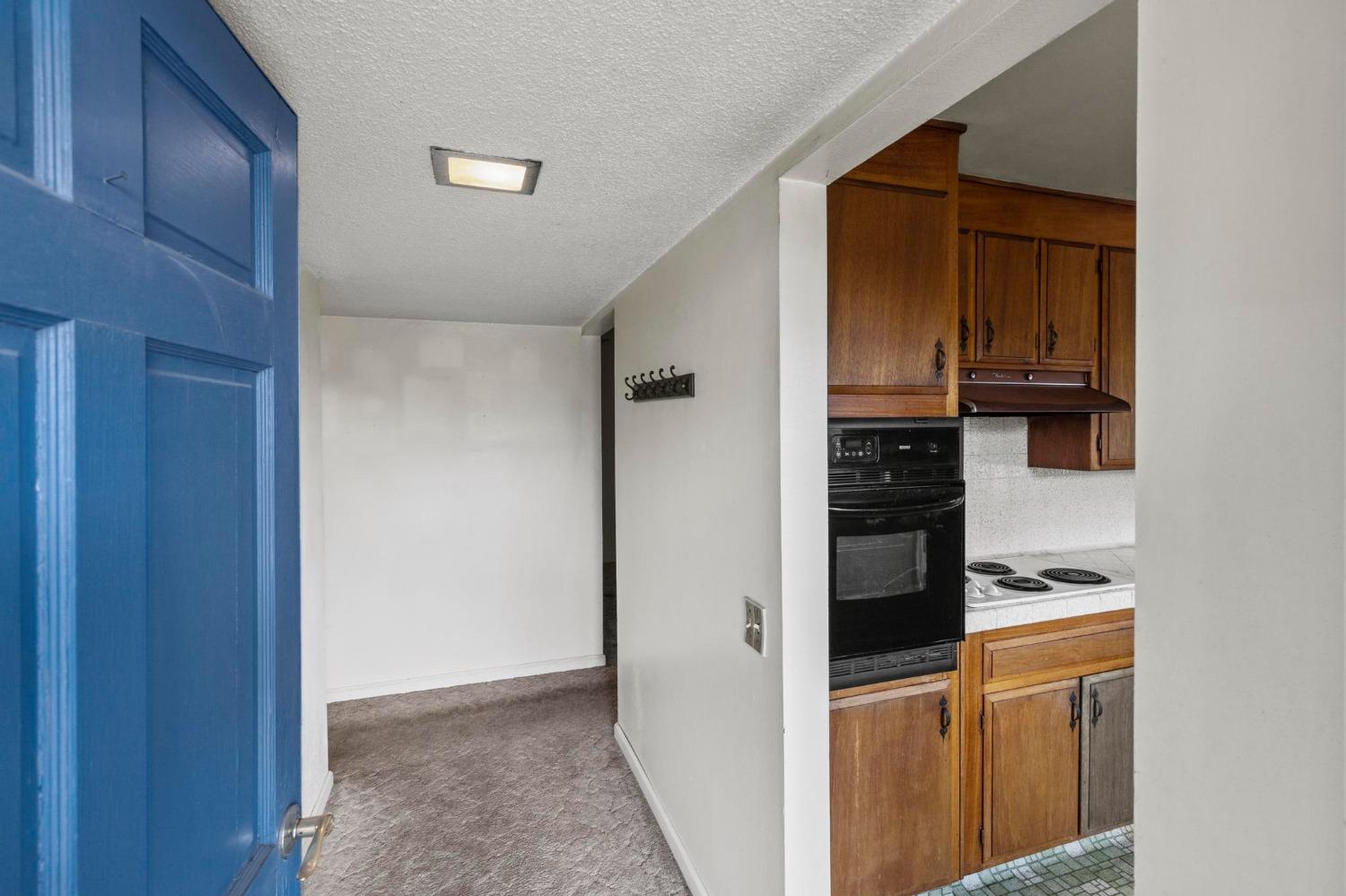 Kitchen with wood cabinets and black appliances beside a carpeted hallway and open blue door.