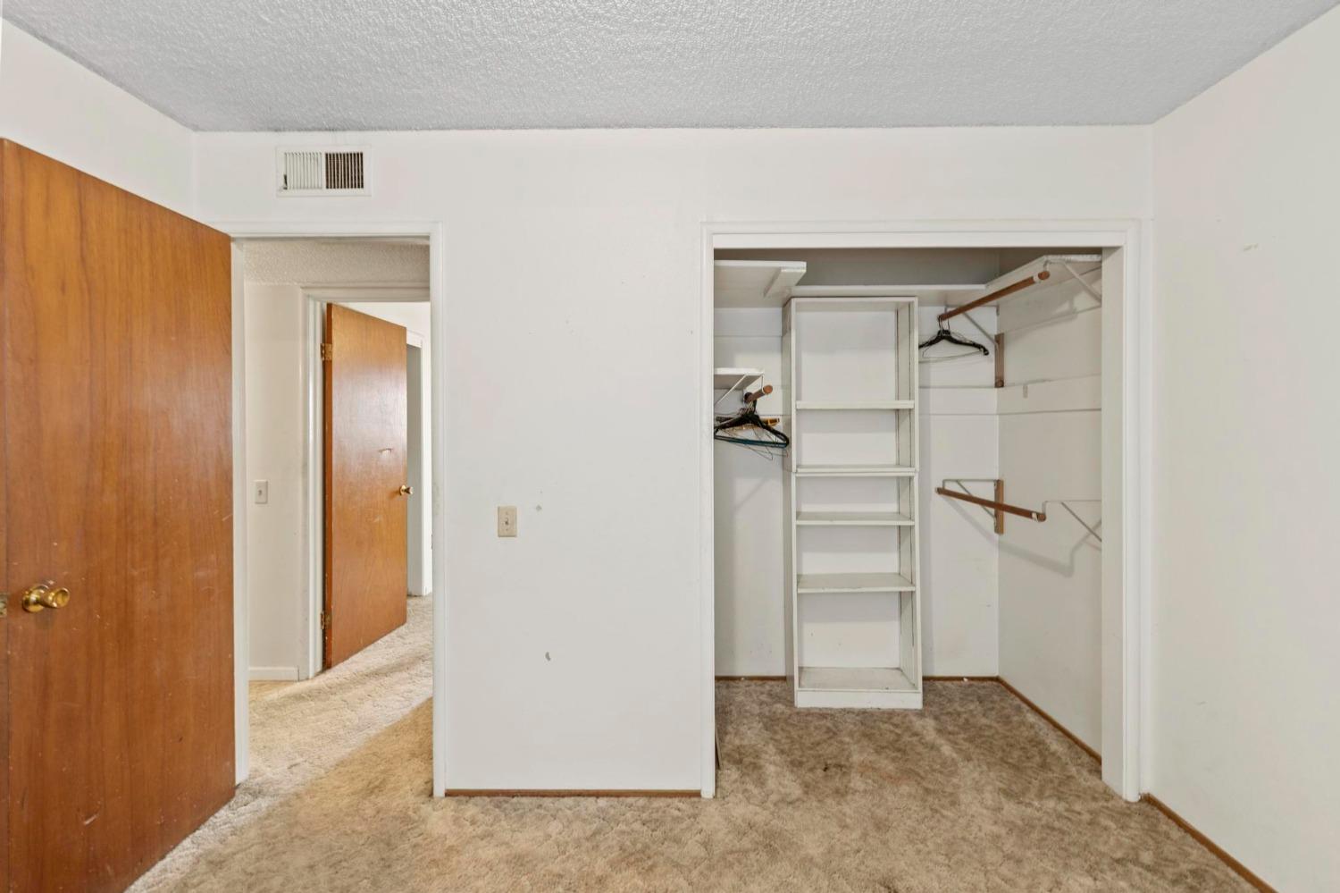 Open walk-in closet with built-in shelves and hanging rods, beside a carpeted doorway.