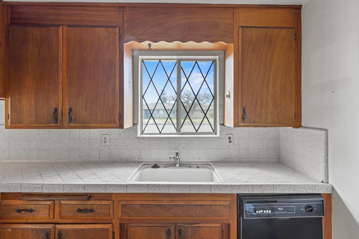 Kitchen with wood cabinets, tiled counters, and a sink beneath a diamond-pane window.