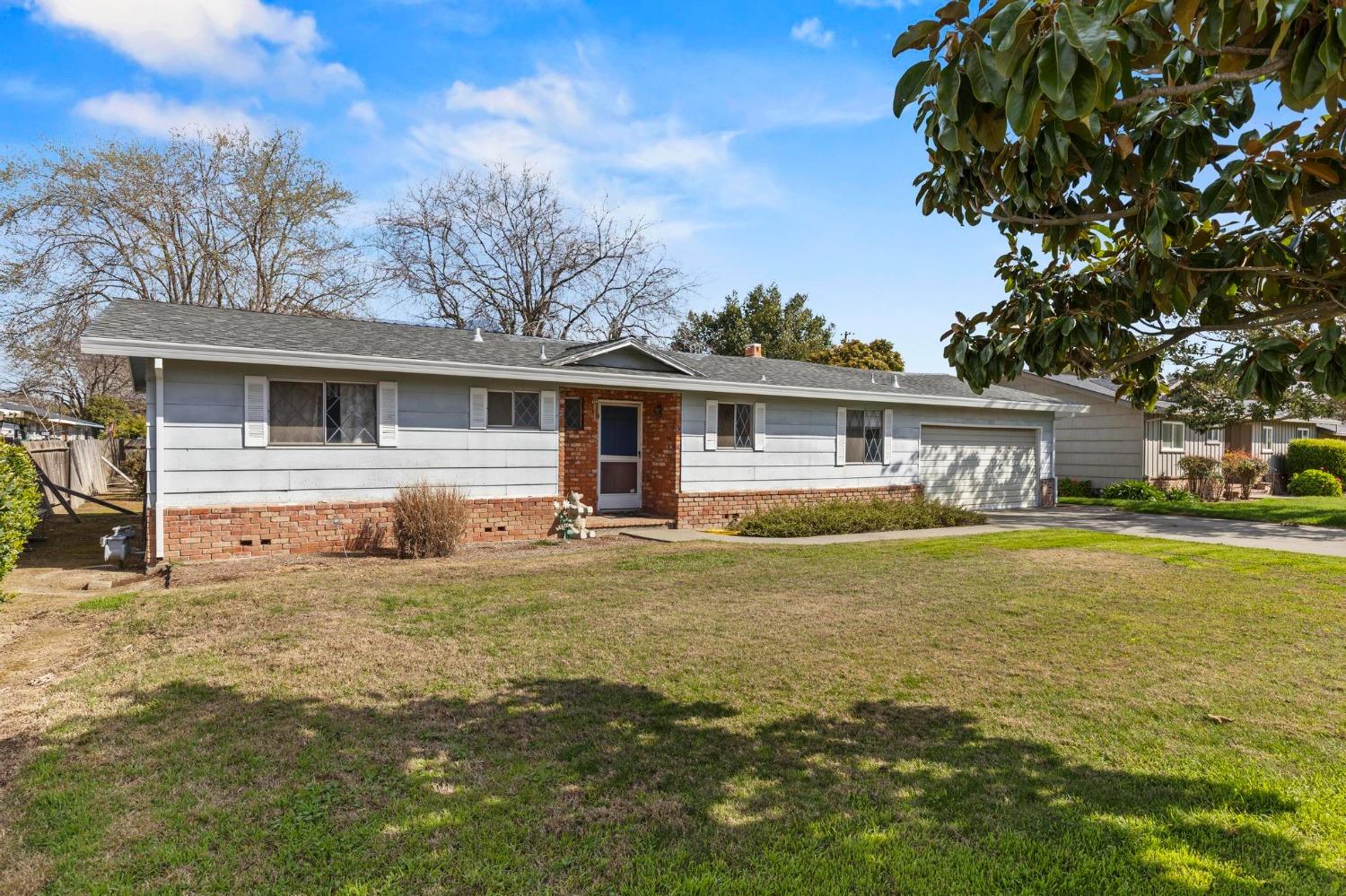 Single-story gray ranch house with a brick entry, attached garage, and broad front lawn.