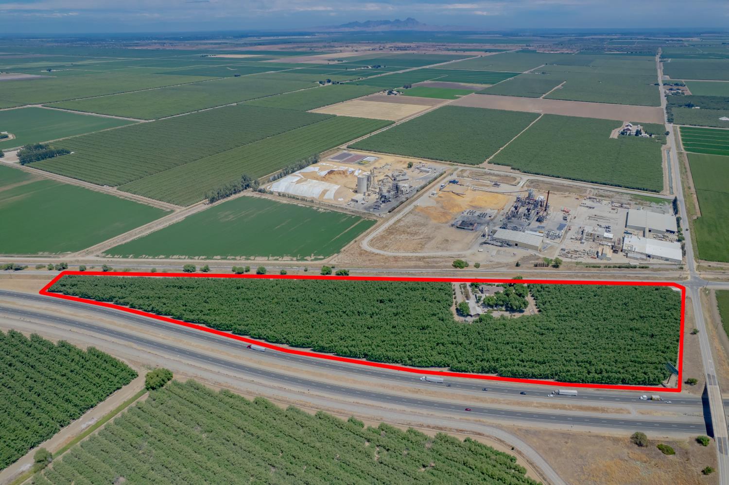 Aerial view of a tree-covered parcel outlined in red beside a highway and agricultural fields.