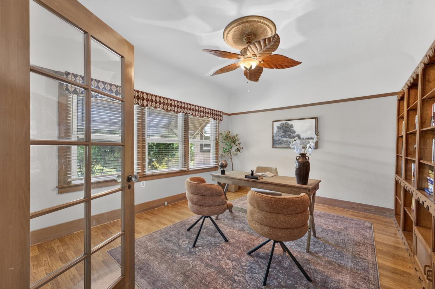 Staged home office with a wooden desk, two chairs, and built-in bookshelves.
