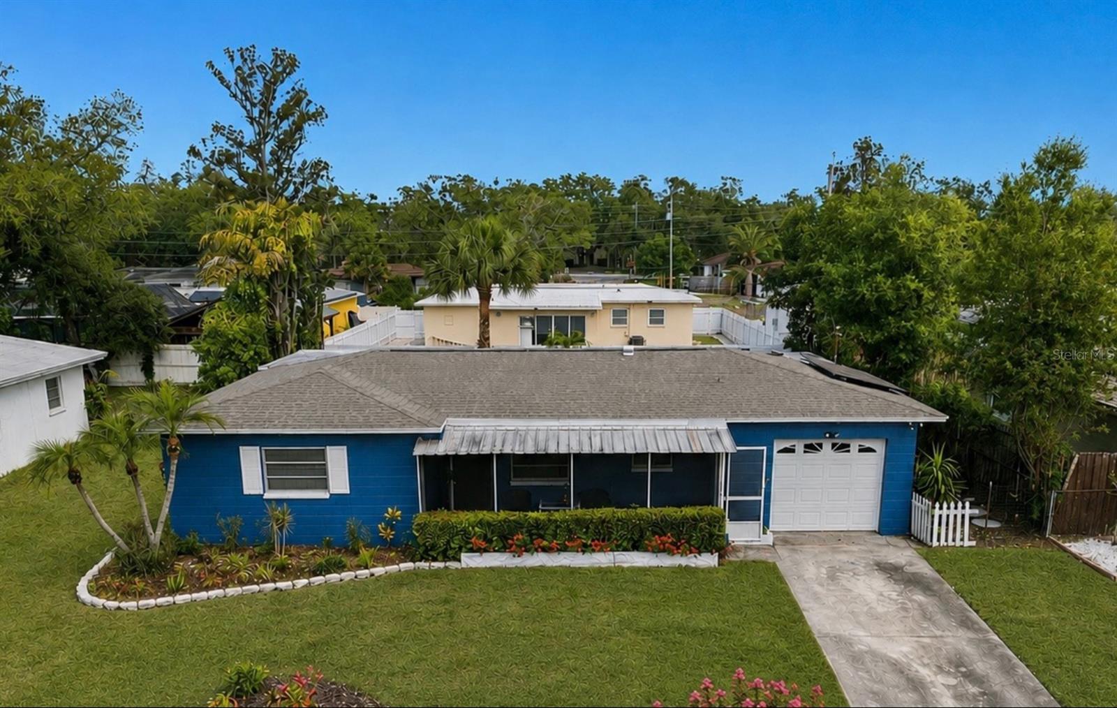 Blue single-story house with a white garage, landscaped front lawn, and paved driveway.