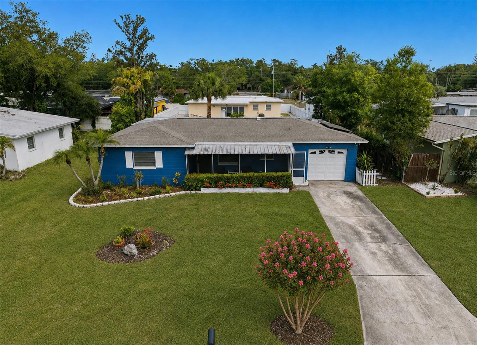 Blue single-story house with a white garage, covered porch, landscaped lawn, and long concrete driveway.