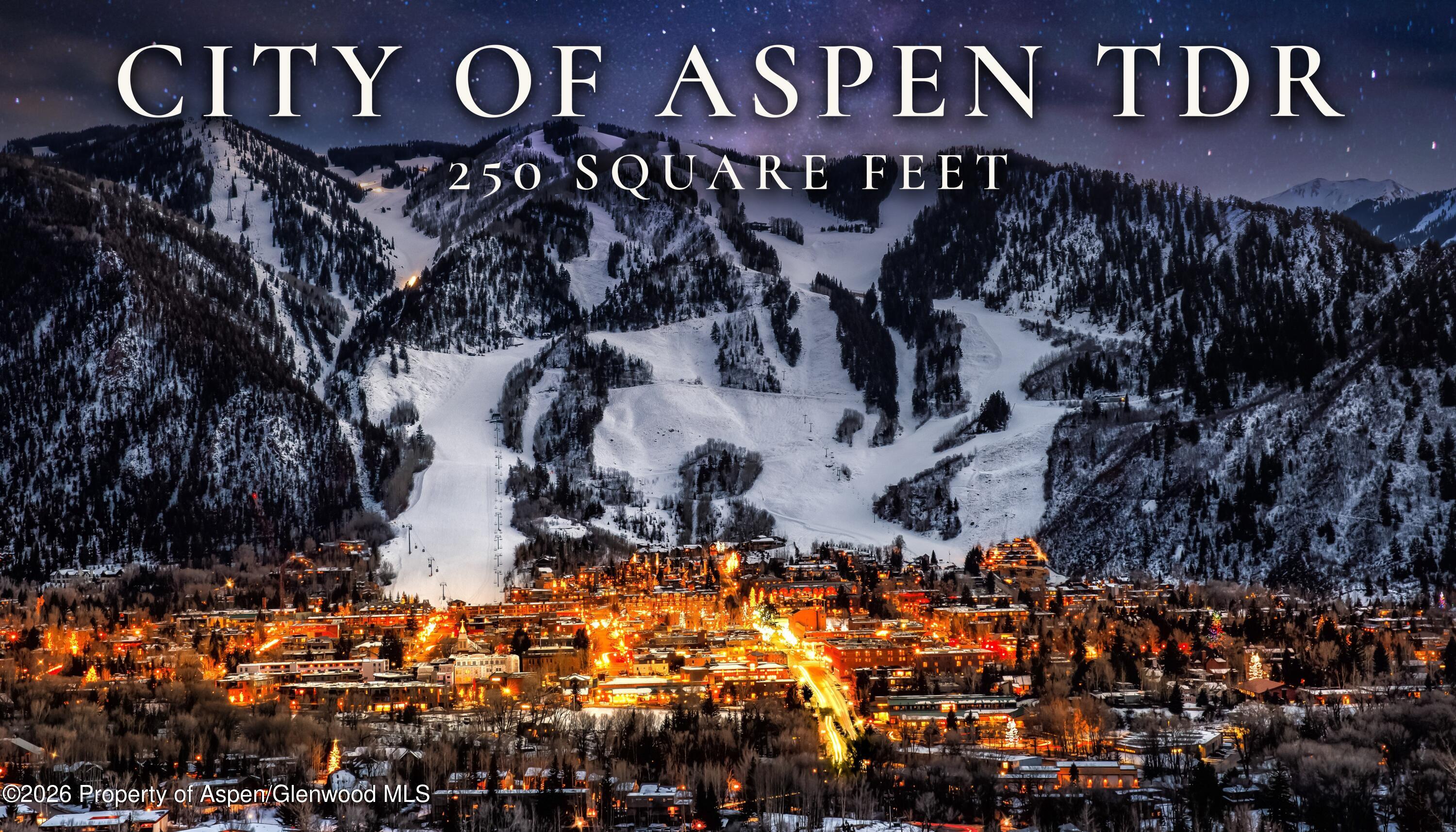 Aspen at night beneath snow-covered ski slopes, with the town glowing below.