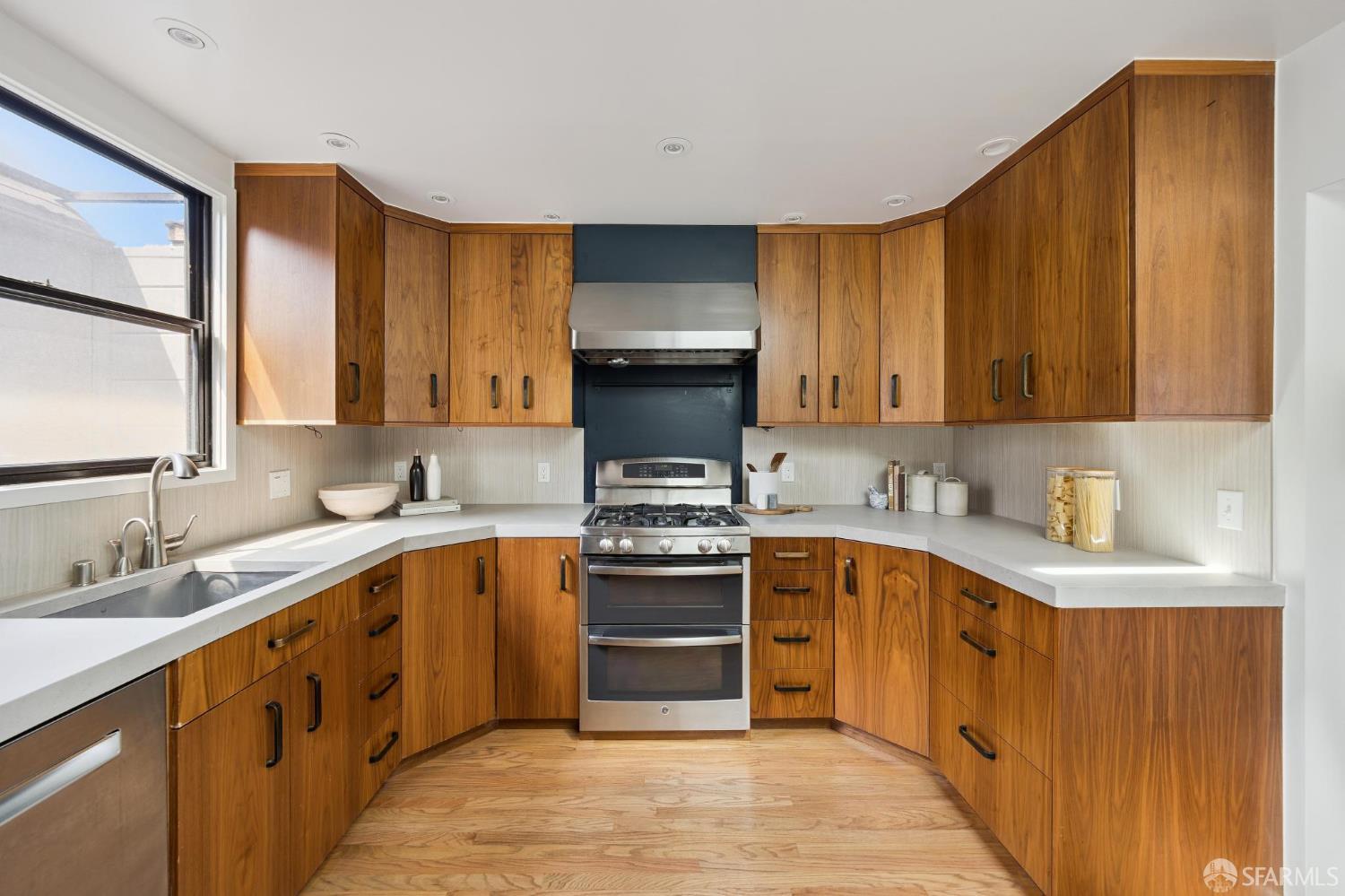 Kitchen with warm wood cabinetry, white countertops, and a stainless steel range beneath a prominent hood.