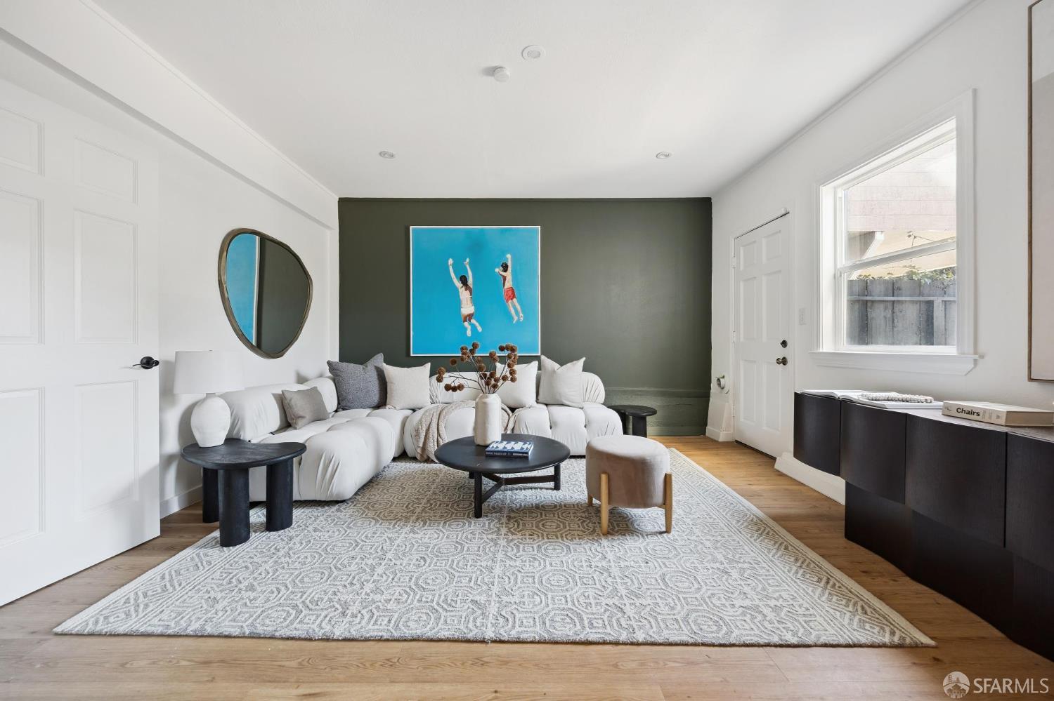 Staged living room with white sectional, dark green accent wall, blue artwork, and patterned rug.