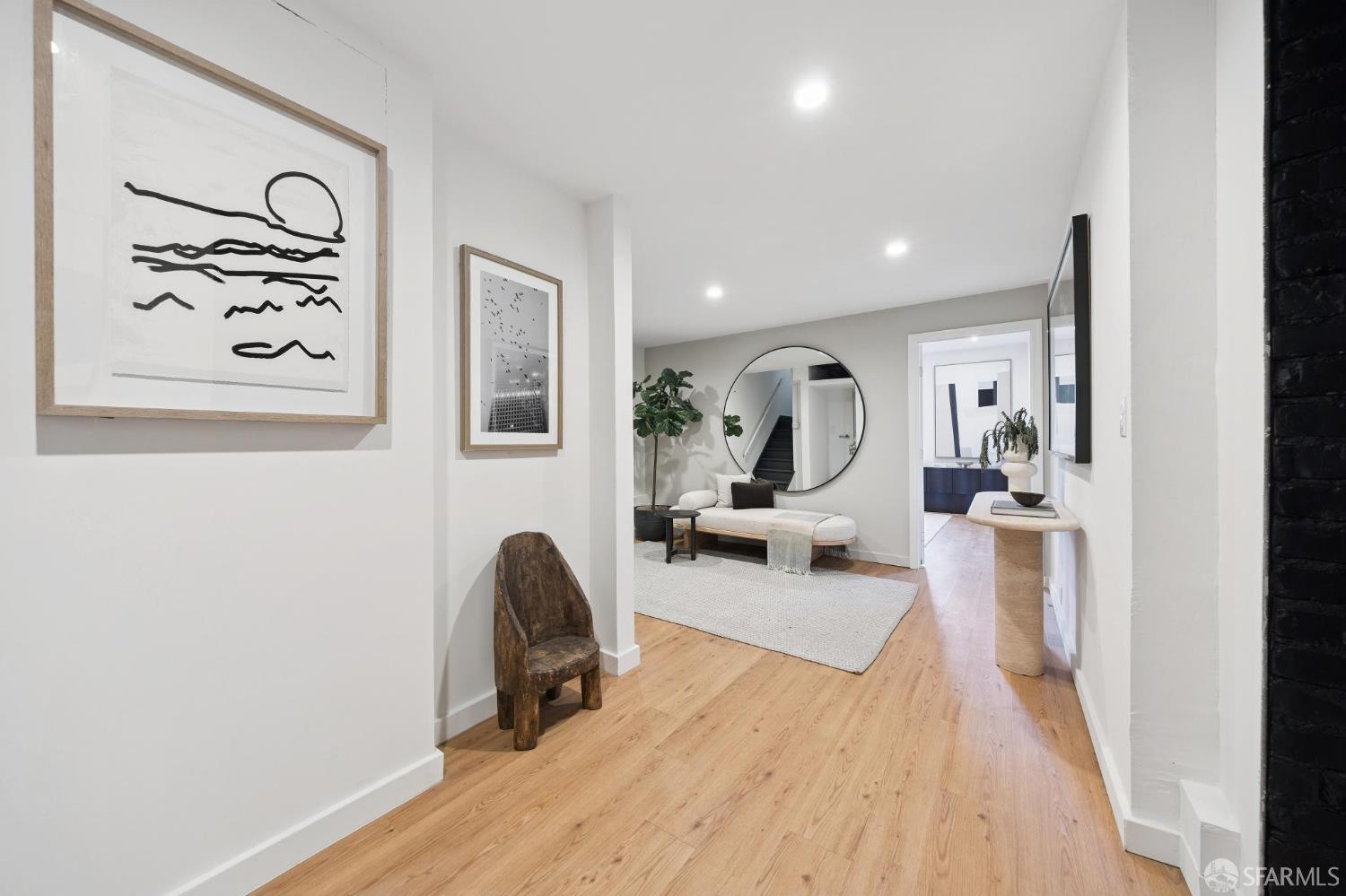 Entry hall opening to a sitting area with a cream sofa, round mirror, staircase, and light wood floors.