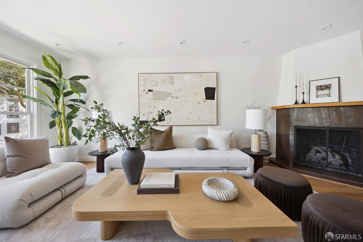 Staged living room with a white sofa, sculptural wood coffee table, and dark tiled fireplace.