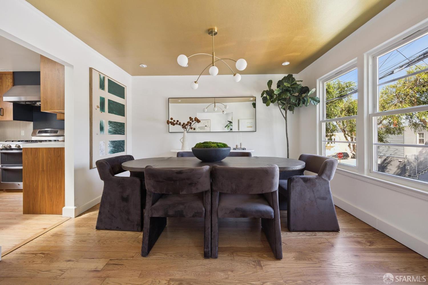 Staged dining room with a round table, gold ceiling, large windows, and an open kitchen.