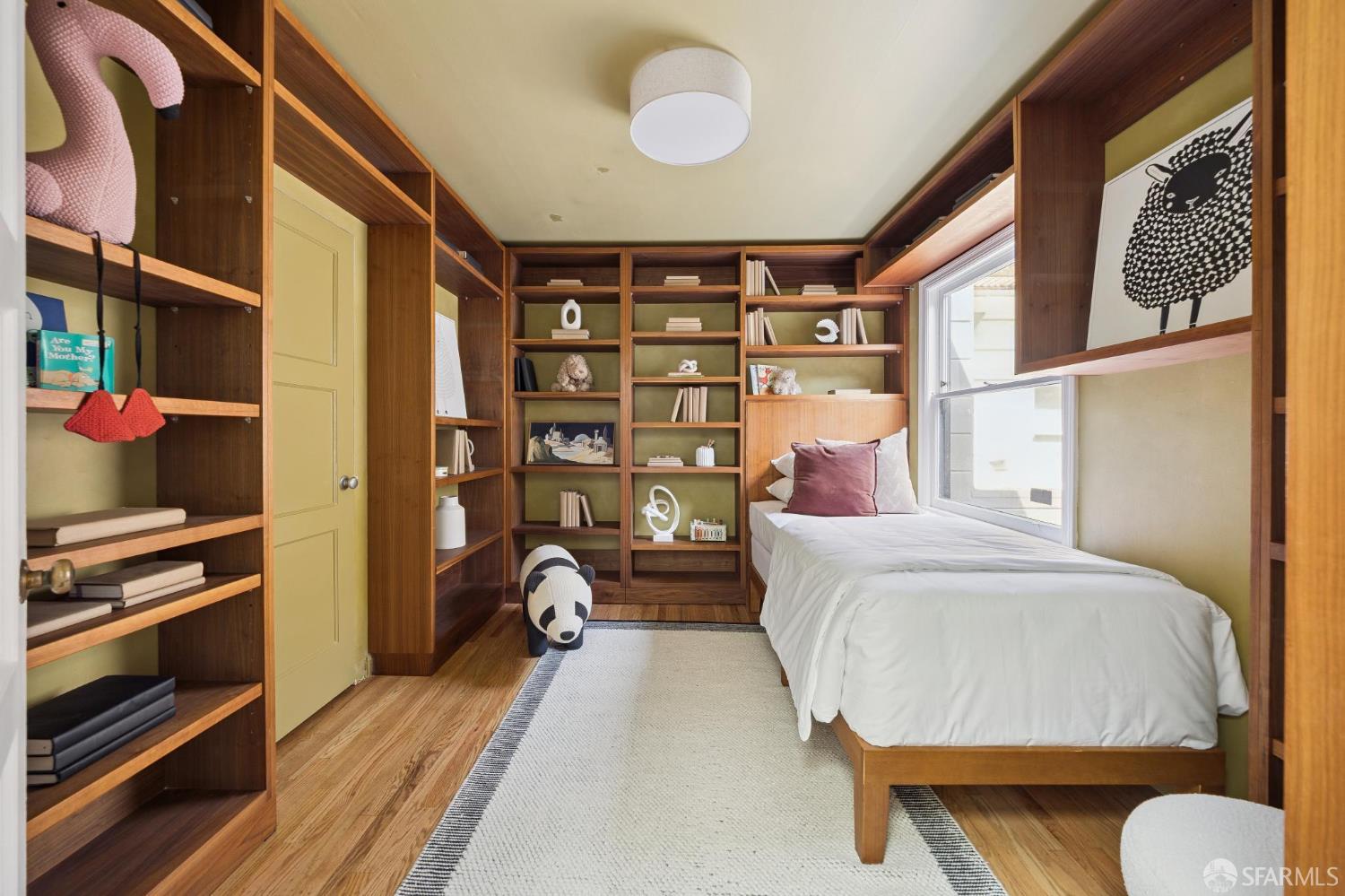 Bedroom with a single bed, extensive built-in wood shelving, and a large window.